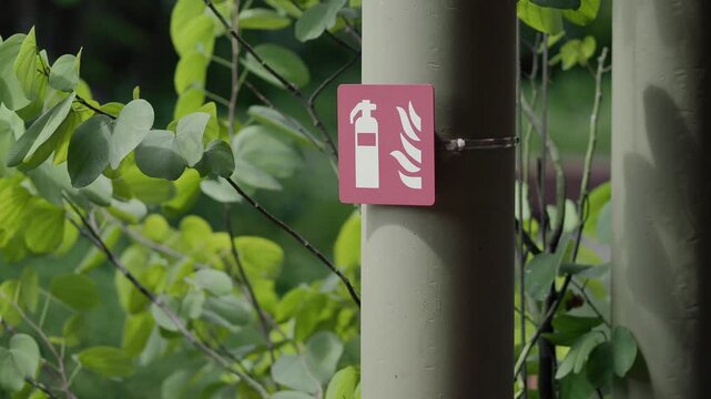 Fire extinguisher marker on a post among trees at a green outdoor site