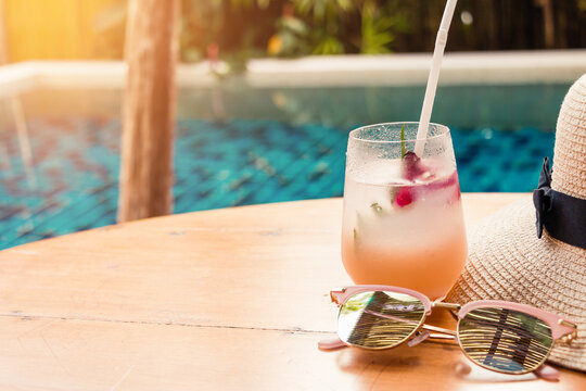 Lychee soda cocktails sunglasses and straw hat on table with blurred poolside background. Summer drinks concept.