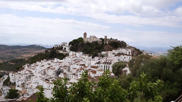 wide angle landscape view of casares, a traditional spanish whitewashed pueblo blanco clinging to a rocky hill topped with an old church under a cloudy sky in Malaga, andalusia, spain.