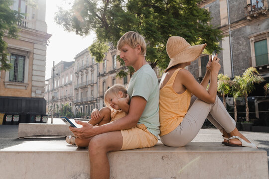 Young family scrolling on phones in a European city