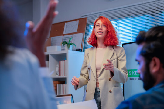 Redhead businesswoman presenting ESG sustainability reporting and rating distribution charts on screen to multiethnic team with laptops and wind turbine model in office