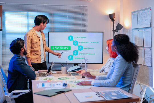 Asian businessman presenting five key steps of ESG reporting process on screen to multiethnic colleagues during sustainability strategy meeting in office