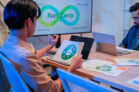 Asian businessman reading ESG report infographic in front of net zero carbon accounting and carbon credit presentation on screen during office meeting
