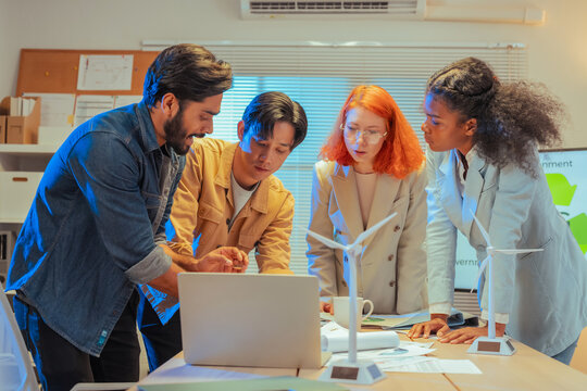 Multiethnic business team standing around meeting table and reviewing ESG sustainability documents and charts together while planning green strategy in office at night