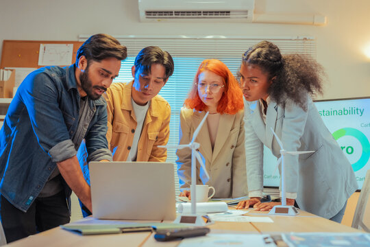 Multiethnic business team standing around meeting table and reviewing ESG sustainability documents and charts together while planning green strategy in office at night