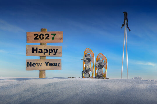 wooden sign with text happy new year in the snow next to snowshoes and ski sticks
