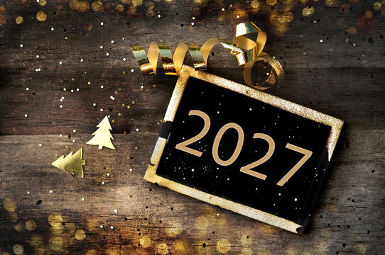 golden 2027 written on  little board on rustic wooden background illuminated bye lights with golden confetti and ribbon