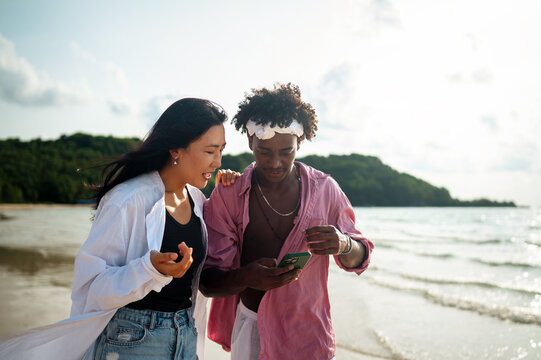 Diverse couple connected, embracing technology and social media while enjoying moments at the beach