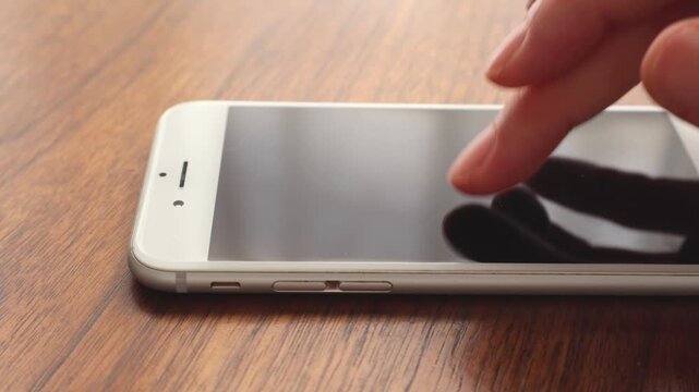 木製テーブルでスマートフォンをタップしている女性の指先のアップ