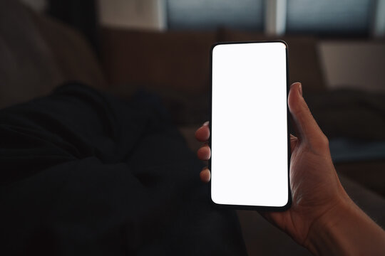 pov shot of man hand hold phone with white screen in dark interior