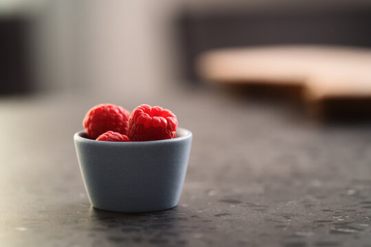 Fresh ripe raspberries in small blue bowl on concrete countertop