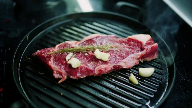 Raw beef steak with rosemary and garlic on a cast iron grill pan as smoke rises, French Riviera, France.