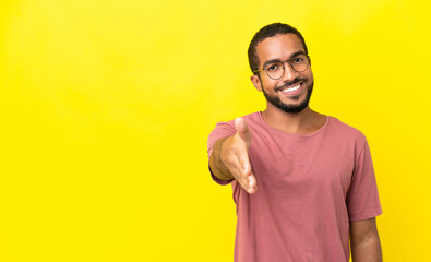 Young latin man isolated on yellow background shaking hands for closing a good deal © luismolinero