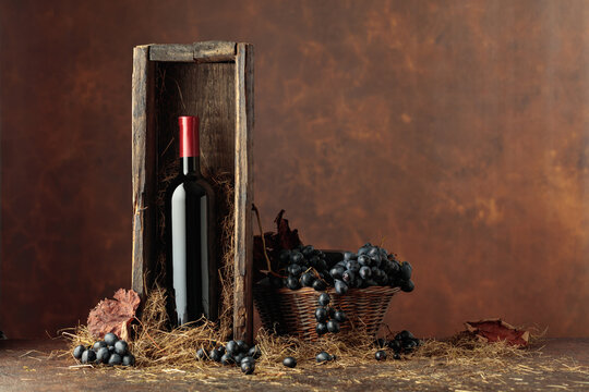 Bottle of red wine in old wooden box and blue grapes in basket.