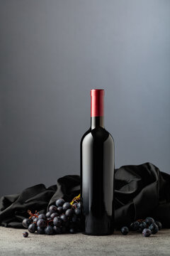 Bottle of red wine with grapes on a grey background.