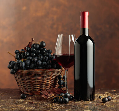 Bottle of red wine and blue grapes in old basket.