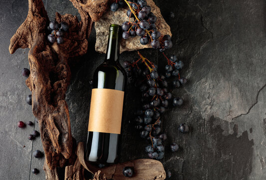 Bottle of red wine with stones, dried snags, and blue grapes.