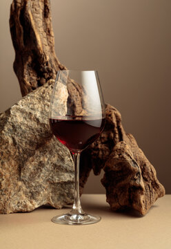 Glass of red wine with old driftwood and a piece of granite rock on a beige background.