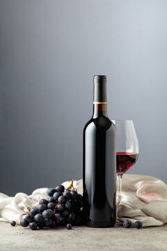 Bottle of red wine with grapes on a grey background.