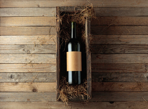 Bottle of red wine with empty label in an antique wooden box with hay.