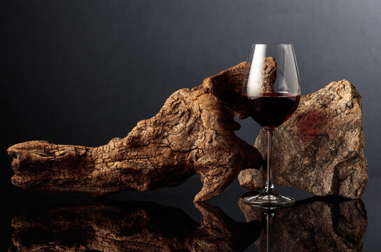 Glass of red wine with old driftwood and a piece of granite rock on a black reflective background.