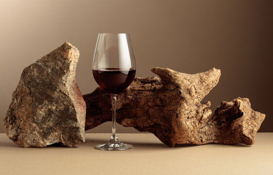 Glass of red wine with old driftwood and a piece of granite rock on a beige background.