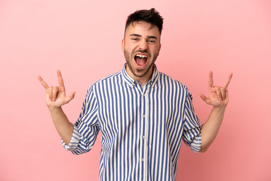 Young caucasian man isolated on pink background making horn gesture
