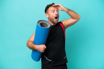 Middle age sport man going to yoga classes while holding a mat isolated on blue background doing surprise gesture while looking to the side © luismolinero