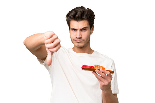 Young caucasian man holding sashimi over isolated background showing thumb down with negative expression