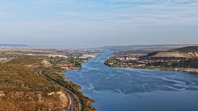 A broad river estuary runs between wooded banks, roads, and settlements near the coast, viewed from above during daylight.