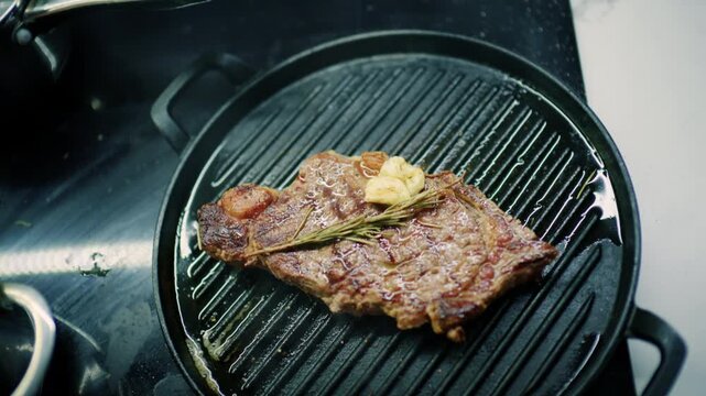 High angle view of a seared beef steak with grill marks, rosemary and garlic butter on a round grill pan, French Riviera, France.