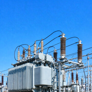 Electrical substation equipment with transformers and insulators against a clear blue sky, power infrastructure close-up