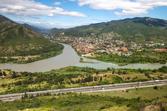 High angle panoramic view of the confluence of two rivers Mtkvari Kura and Aragvi with the historic town of Mtskheta surrounded by green mountains in Georgia.