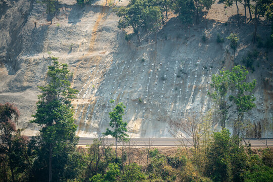 Work to strengthen mountain slope from landslide and soil fall with special metal mesh, geoprotection and geological work for safety using netting preventing rockfall from hill on road and life damage
