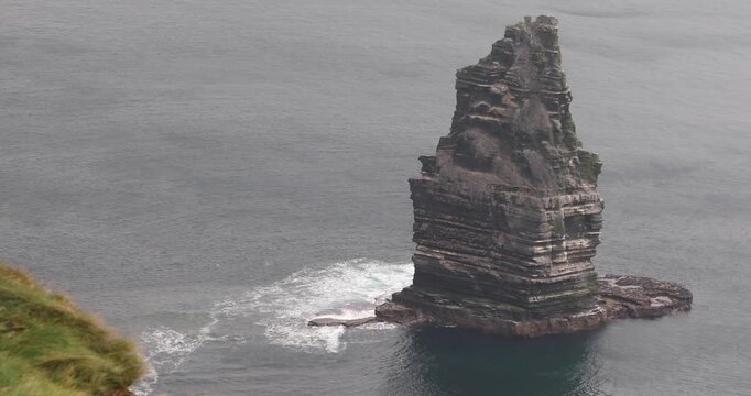 Branaunmore sea stack rises from the Atlantic at Ireland&rsquo;s Cliffs of Moher, displaying dramatic layered rock formations as waves break around its base beneath an overcast sky.