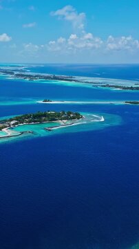 Aerial establishing view of luxury tropical resort islands in crystal clear ocean water. Ideal backdrop for honeymoon promo, hydroplane in the sky, vertical video