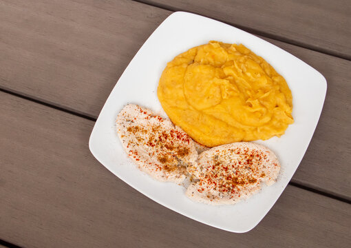 Plato de comida con dos filetes de pechuga de pollo y pure de verduras. Plato de comida servido sobre una mesa de madera de filetes condimentados con especias y pure de patata y zanahoria.