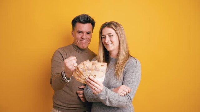 Smiling man and woman holding and counting a fan of fifty euro banknotes. Successful people celebrating their profit against a yellow background