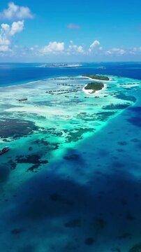 Stationary aerial view of a luxury resort hotel on a tropical island in the Maldives, surrounded by clear blue waters and vibrant coral reefs in a peaceful scene.vertical video