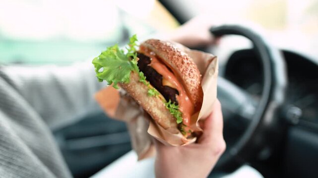 Woman presents freshly made burger from driver seat. Car interior and handheld meal create relatable lifestyle footage for food brands.