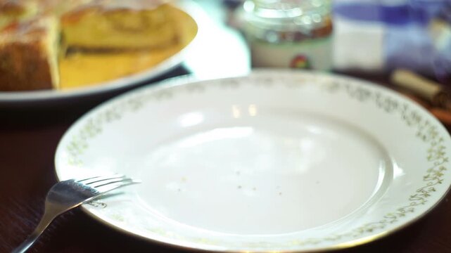 Hand taking apple cake piece closeup. Empty plate crumbs fork, sweet temptation.