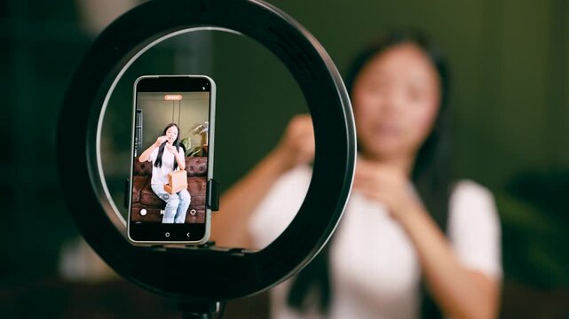 Asian content creator live streaming an unboxing video. Professional influencer filming a vlog at home with a smartphone and ring light