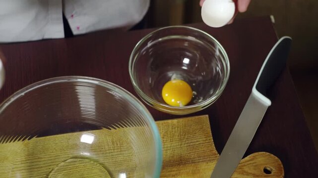 Cook pouring raw yolk from eggshell into bowl. Close up homemade dessert recipe.