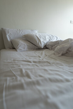 Unmade bed with soft linen sheets and cozy blanket. A serene bedroom setting