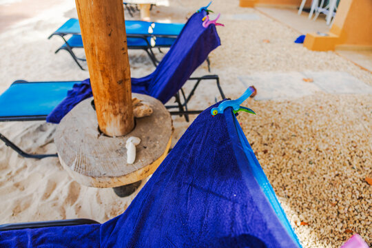 Close-up view of parrot towel clips securing beach towels to sun loungers beside wooden parasol table. Aruba.