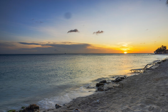 Beautiful view of sunset over Caribbean Sea as gentle waves wash sandy beach beside empty sun loungers. Aruba.
