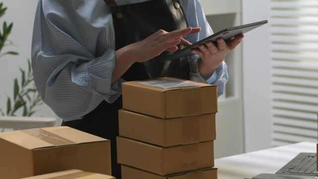 Warehouse clerk using digital tablet to verify delivery orders and package barcodes on shipping boxes.