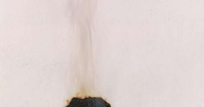White Paper Slowly Smoldering in Macro View. White paper smolders in macro view as blackened areas gradually expand. Burning paper releases delicate smoke and scattered orange embers.