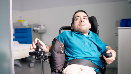 Man with a physical disability operating an electric wheelchair joystick in a hospital setting, reflecting mobility and independence © DMegias