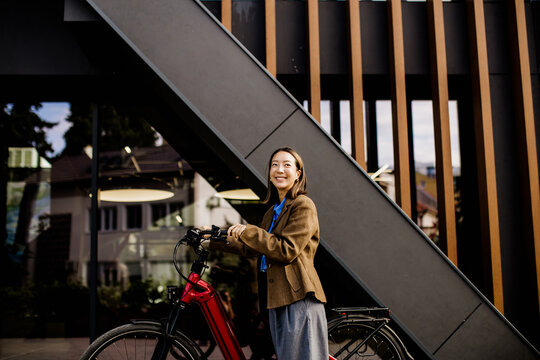 Woman smiles while standing by her electric bike outside a modern building
